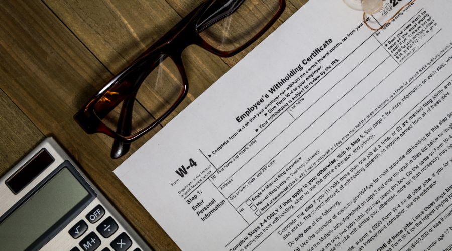 Blank Form W-4, Employee’s Withholding Certificate, beside a calculator and glasses