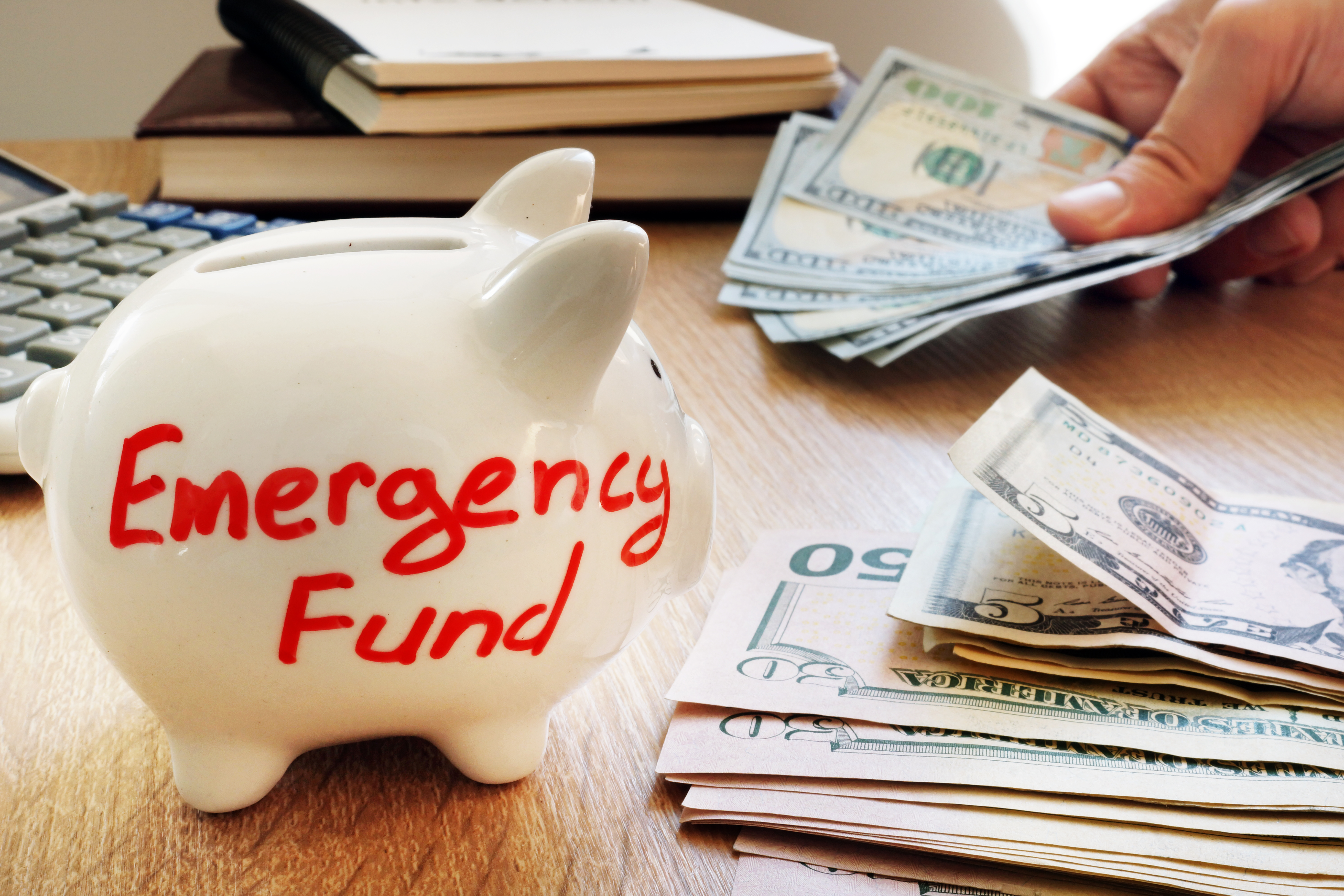 piggy bank with emergency fund written on it next to a pile of money