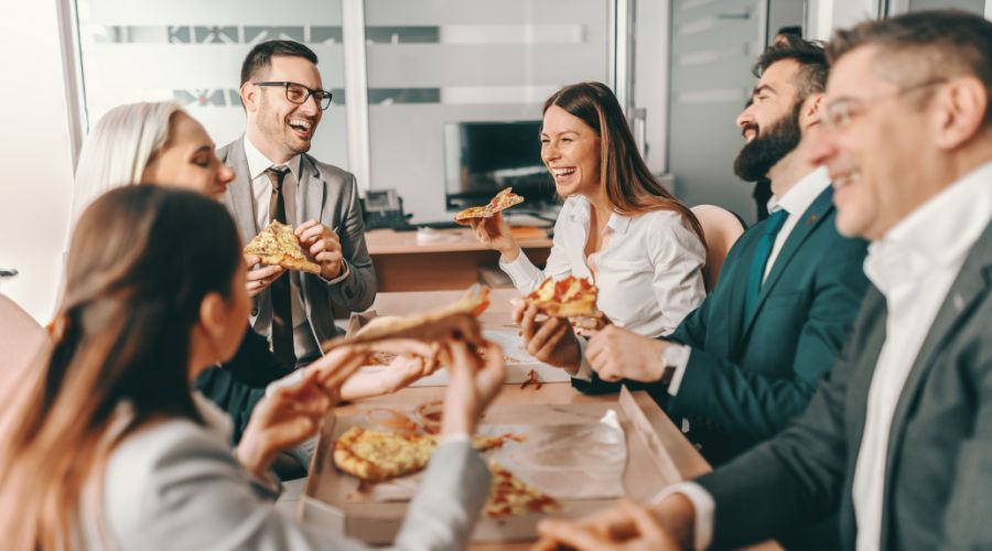 group of coworkers laughing and eating pizza