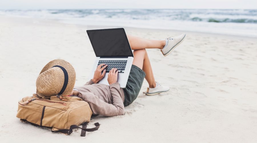 person reviewing time off requests on a laptop while lying on the beach